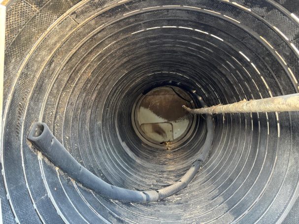 Potato barrel washer booster bar View through a circular black drainage pipe, with dirt and a faint light at the far end.